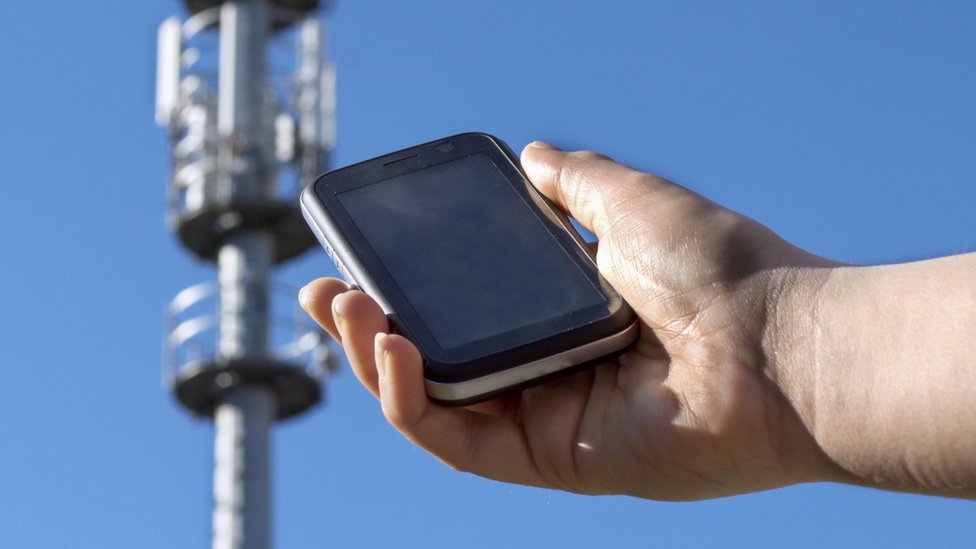 Teléfono móvil frente a una torre de antena de celular.