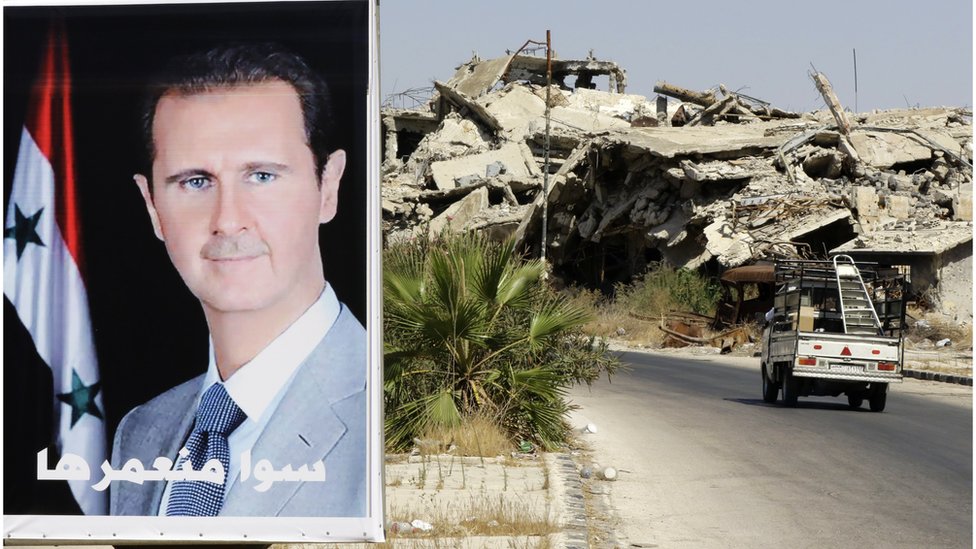 Un poster con el rostro de Bashar al Asad junto a un edificio destruido