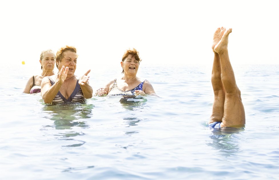 Un grupo de mujeres se divierten en el agua. Una se para de manos.