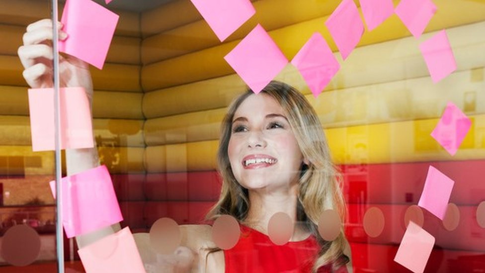 Muy pocos trabajos te harán usar toda tu energía creativa. Es una realidad que hay que aceptar, recomiendan los expertos. Una mujer haciendo un corazón de post its en un vidrio de una oficina