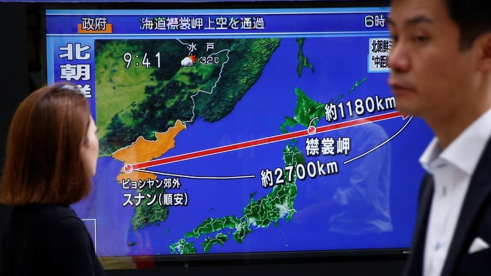 People walking in front of Japanese TV showing missile flight path