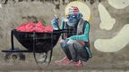 Mural shows a blue man enjoying a cigarette sitting by a wheelbarrow full of hearts 