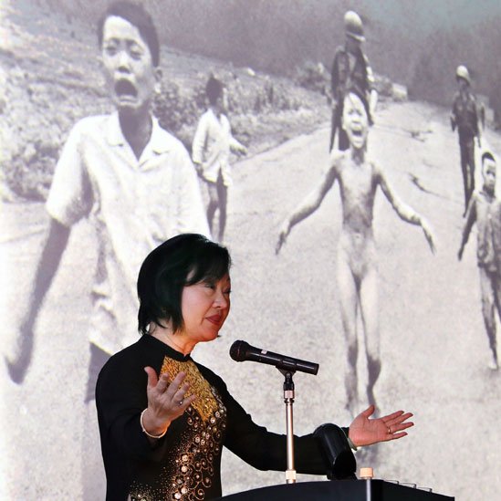 Kim Phuc hablando en una conferencia, detrás de ella está proyectada la foto que tomó Nick Ut en 1972