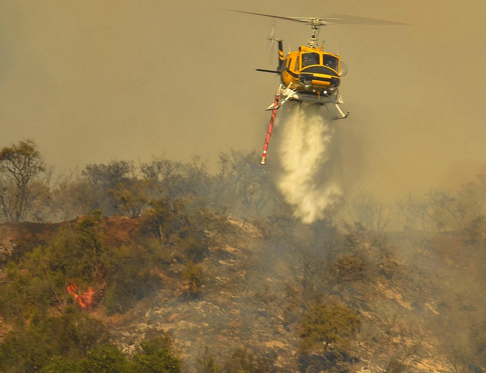 Helicóptero rociando agua sobre incendio