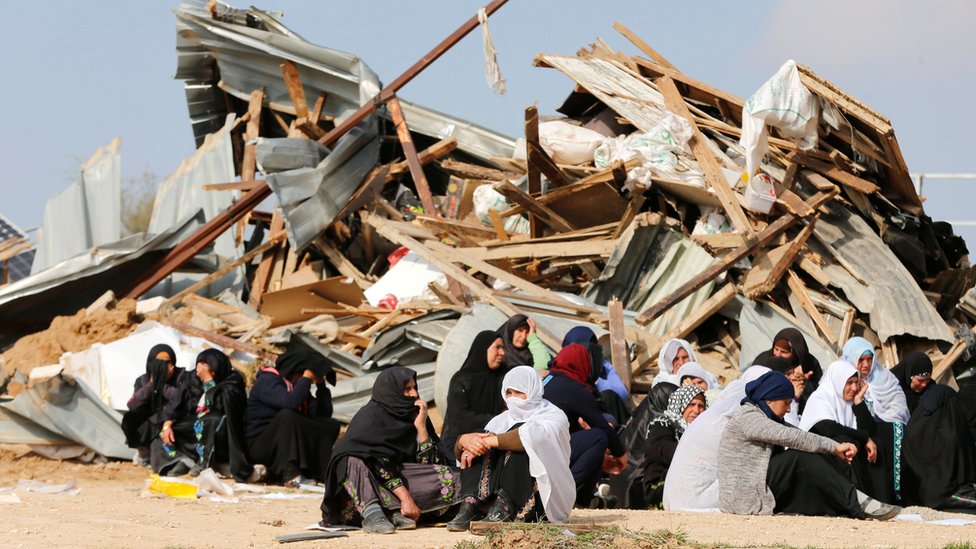 نساء فلسطينيات يجلسن جوار منزل مدمر