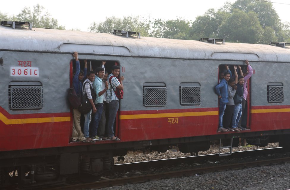 People hang onto local trains as the commuter train enters Mumbai