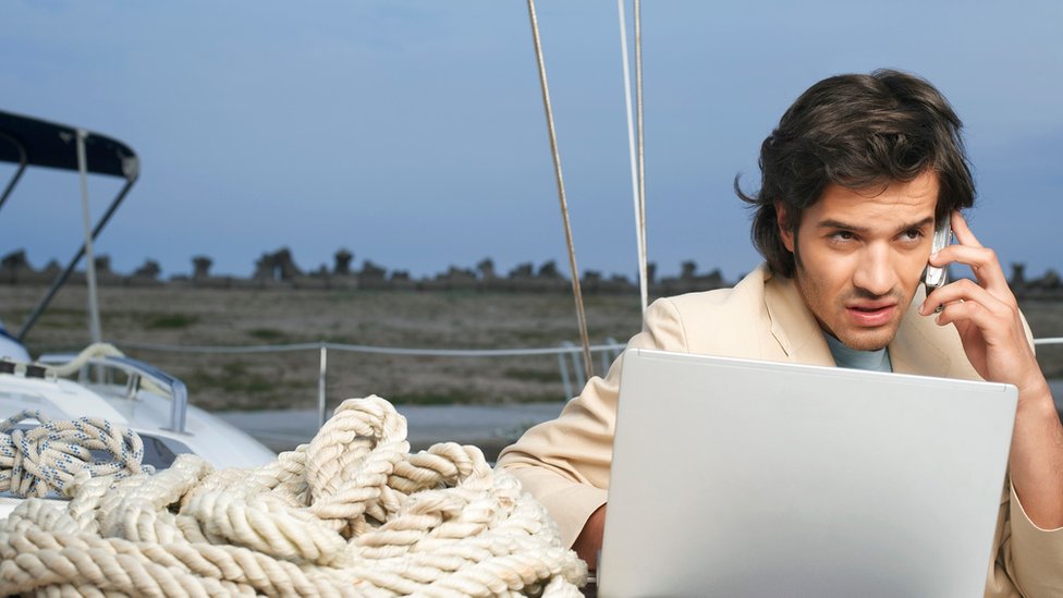 Un hombre que trabaja en su laptop entre cuerdas de navegación (de vacaciones)