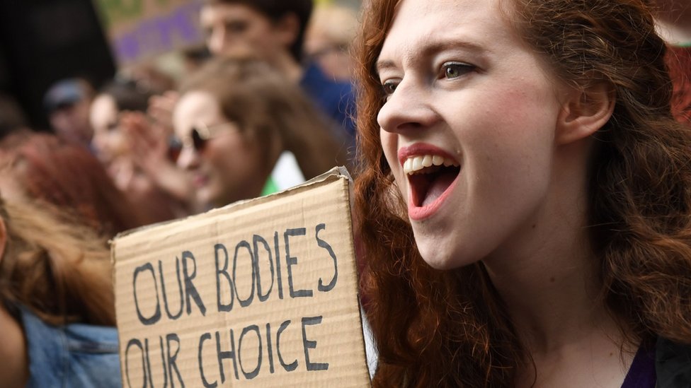 Una mujer en una manifestación sostiene un cartel que dice: 