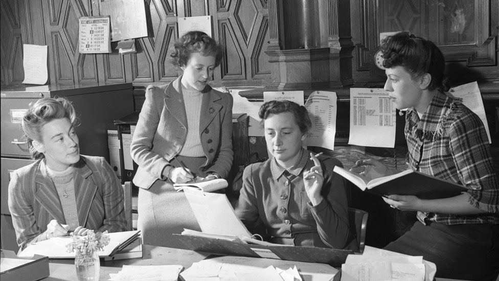Integrantes del equipo administrativo del Servicio Latinoamericano I. V. Mallett, C. M. O'Callaghan, E. Ware, R. Canter, cuator mujeres jóvenes conversando en torno a un escritorio
