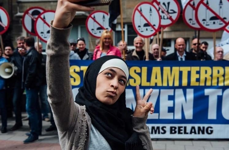 Photo of Zakia Belkhiri taking a selfie with Vlaams Belang protesters in the background