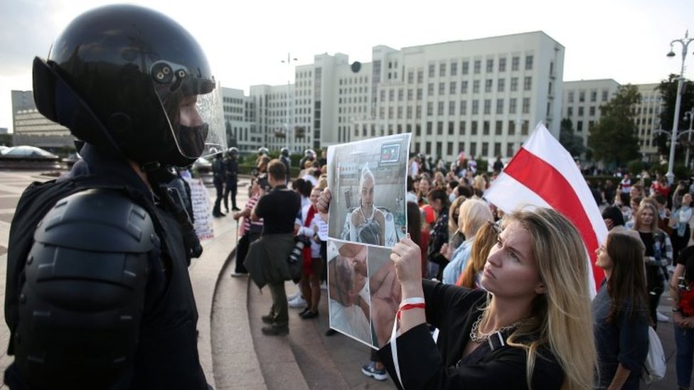 A woman holds pictures of protesters allegedly beaten by police in front of a riot police officer in Minsk, Belarus. Photo: 5 September 2020