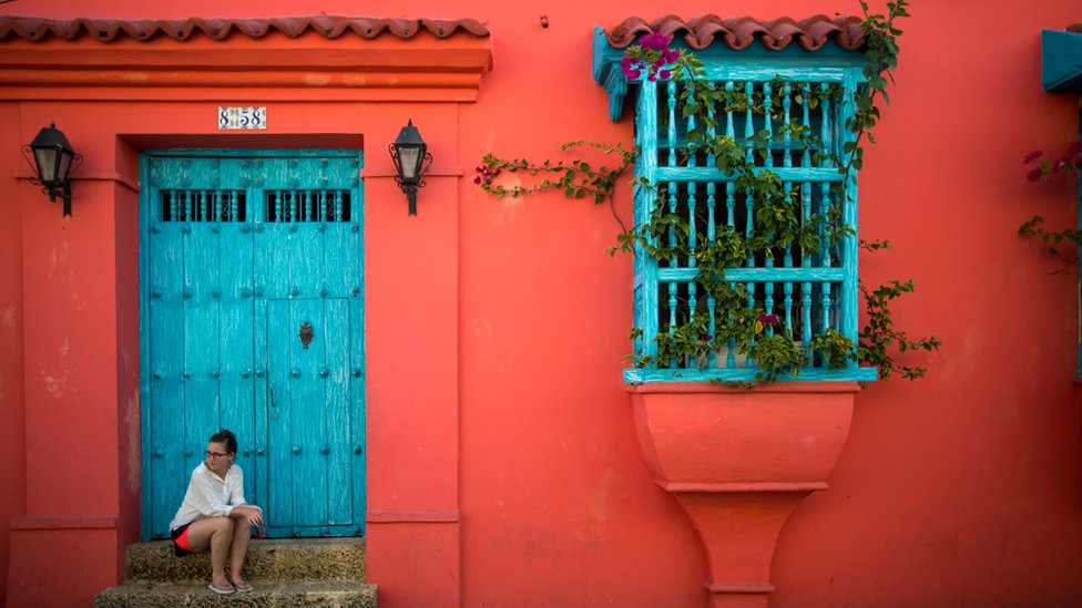 Una mujer está sentada en una escalera en la fachada de una casa del casco colonial de Cartagena de Indias, en Colombia.