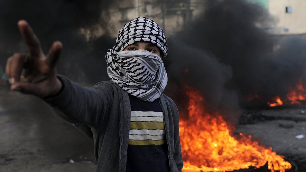 فلسطيني يرفع علامة النصر امام إطار محترق في غزة