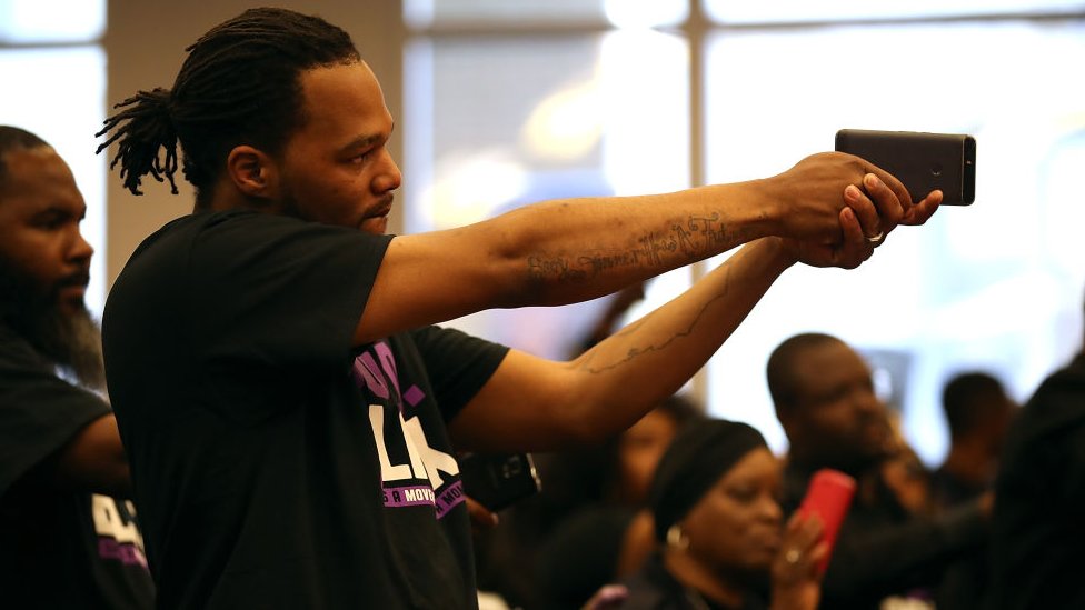 Un asistente a una reunión especial del concejo municipal en Sacramento, California, sostiene un teléfono como si fuera un arma