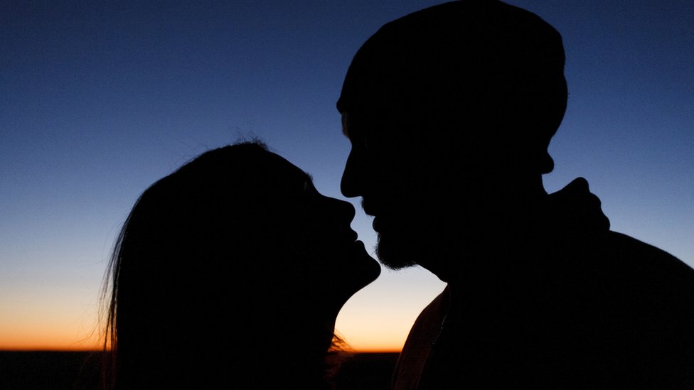 Un hombre y una mujer se besan al atardecer.