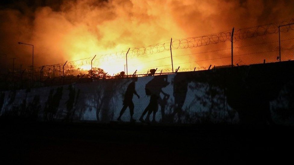 Refugees and migrants carrying their belongings are silhouetted as they flee the fire in Moria in Lesbos on 9 September 2021