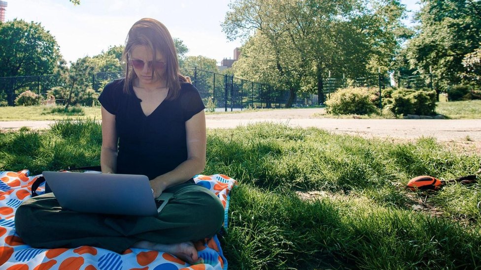 Trabajar fuera de la oficina, si puedes, es un pequeño cambio que puede ayudarte a disfrustrar más tu trabajo. Una joven usando su laptop en un parque