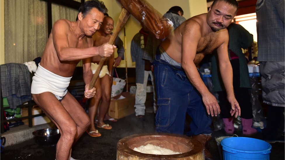 Men in loincloths pounding rice