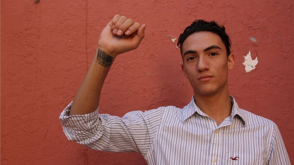 Luis Mercado muestra un tatuaje en su muñeca con un código de barras y la palabra