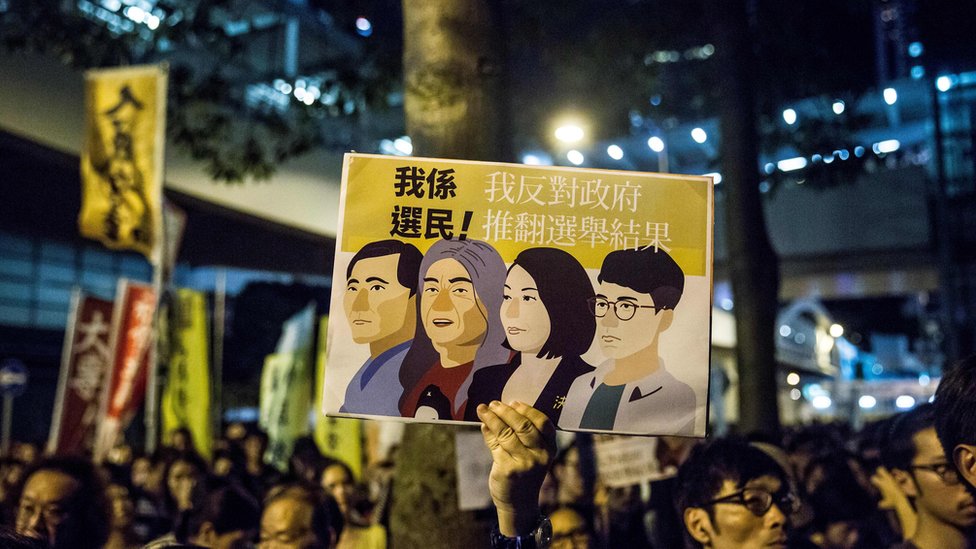 示威者拿著牌子，抗議香港當局取消四名非建制派議員的資格