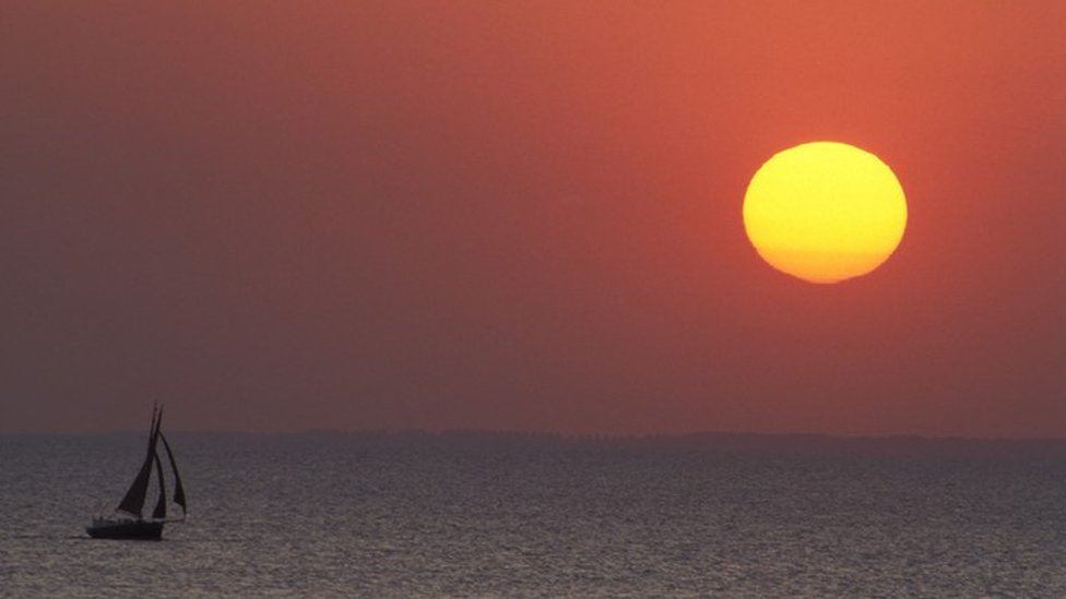 Una embarcación de vela navegando solitaria, con un atardecer de fondo
