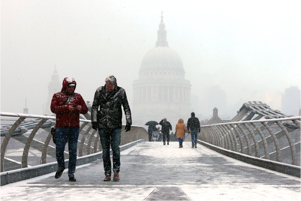 People walk over Millennium Bridge in the snow, in London