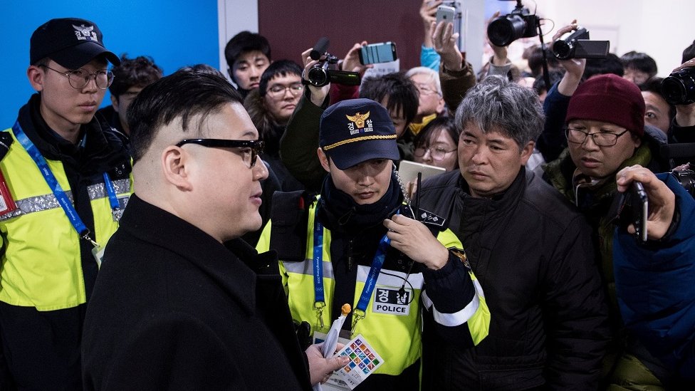 A Kim Jong-un impersonator is surrounded by journalists who try to film him on their cameras and phones