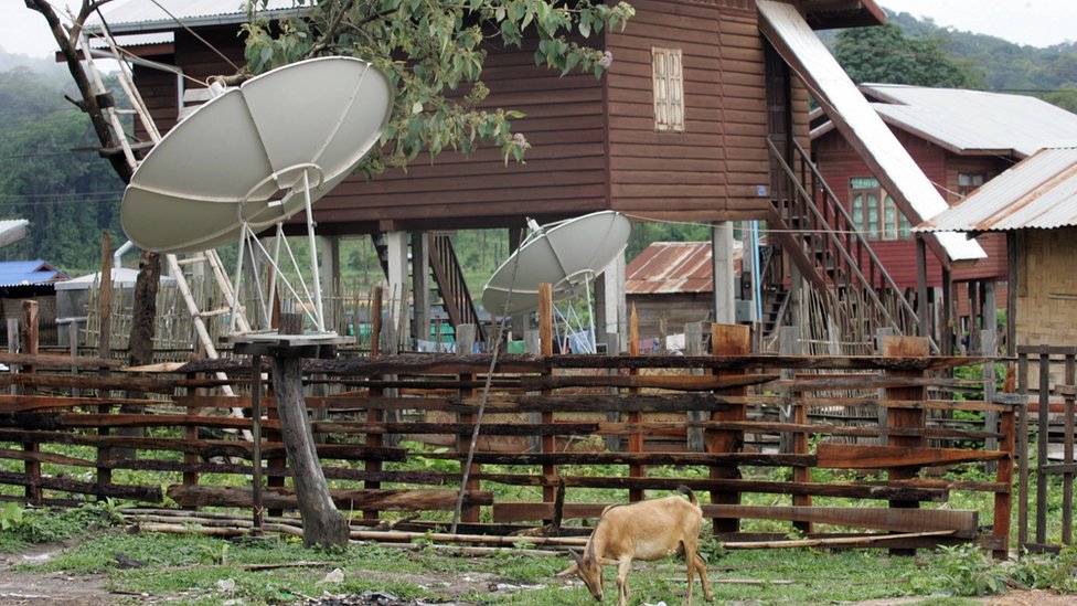 A goat eats grass near by TV satellite dishes installed outside houses at a village in the South-western Nakai plateau in Laos.