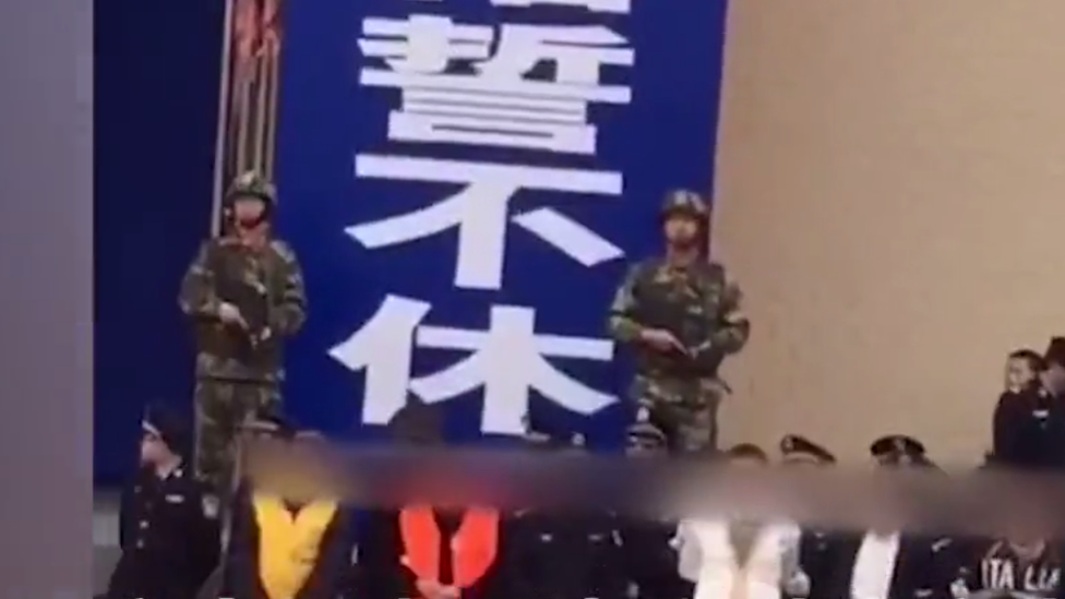 Policías armados se paran detrás de un grupo de gente que esperar oír las sentencias.