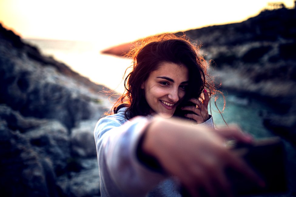 Mujer tomándose un selfie al atardecer.