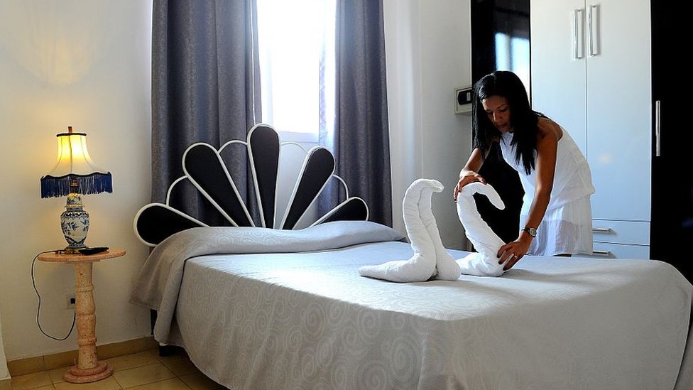 Una mujer arregla unas toallas con formas de cisnes para dejarlas encima de una cama en una posada en La Habana.