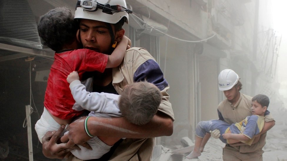 Rescatistas cargando niños en una bombardeada Alepo.