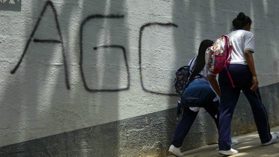 Dos adolescentes caminan frente a un mural con la sigla "AGC" que significa Autodefensas Gaitanistas de Colombia.