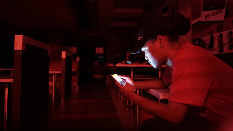 La empleada de un restaurante de comida rápida se ilumina con su celular durante un apagón.