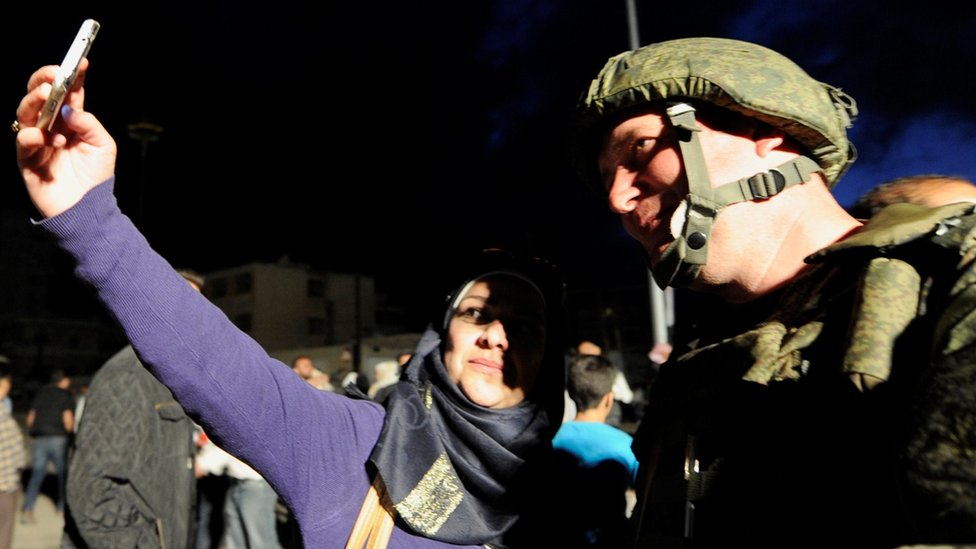 جندي روسي وسيدة سورية تلتقط صورة لها معه