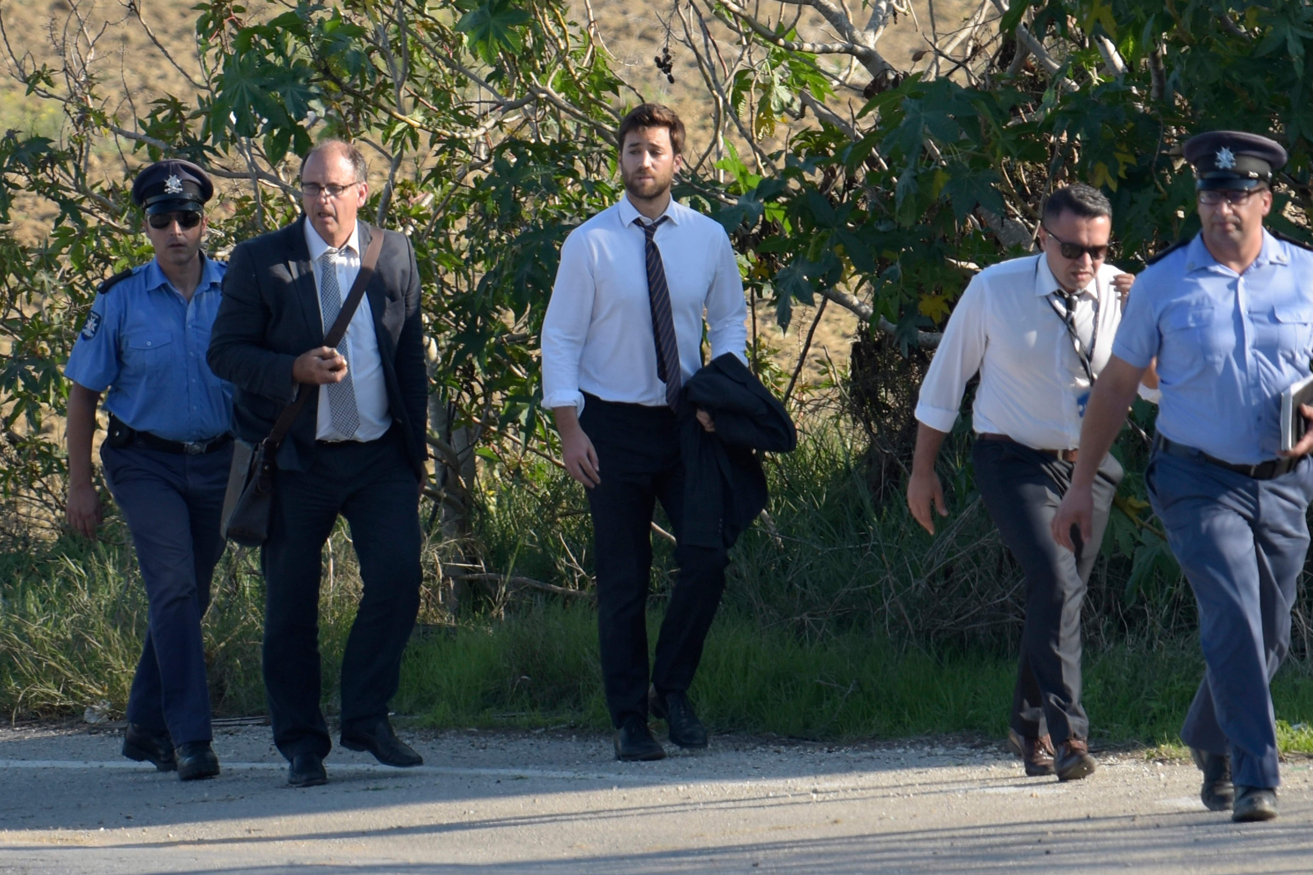 El hijo de la periodista asesinada Daphne Caruana Galizia, Matthew Caruana Galizia (en el centro, con camisa y corbata y el saco en la mano) y su esposo Peter Caruana Galizia (a su izquierda, con gafas y bolso), en la escena del crimen junto a la policía, en Bidnija, Malta, el 16 de octubre de 2017.