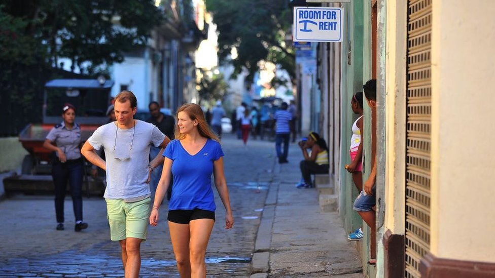 Turistas caminan cerca de una casa que alquila habitaciones para turistas.