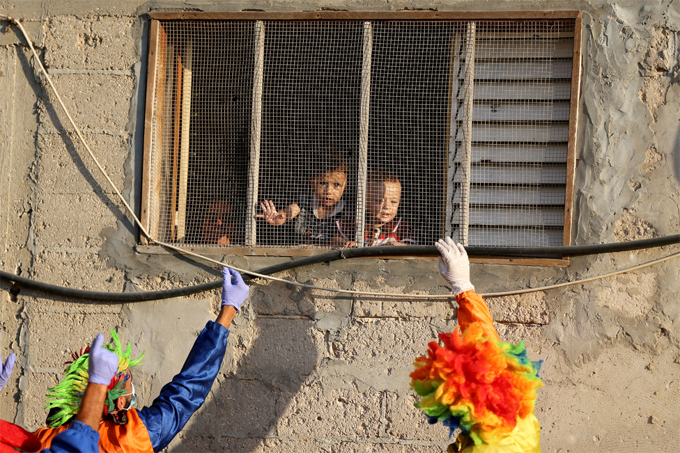 Clowns winken Kindern zu, die aus dem Fenster schauen