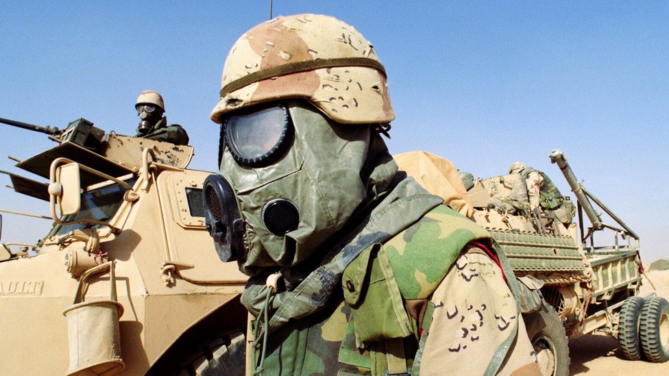 A US soldier (C) stands 09 February 1991 somewhere in Saudi Arabian desert in front of a French armored vehicle (VAB) from the 6th Foreign Legion Engineers Regiment. Both soldiers are wearing chemical warfare equipment.
