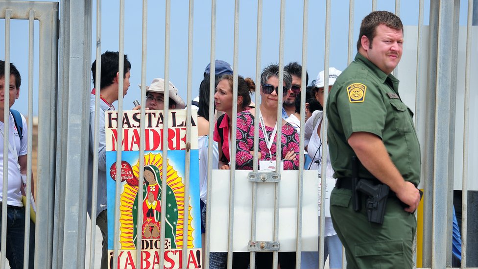 Un guardia fronterizo de EE.UU., junto a mexicanos que protestan en San Diego, California.