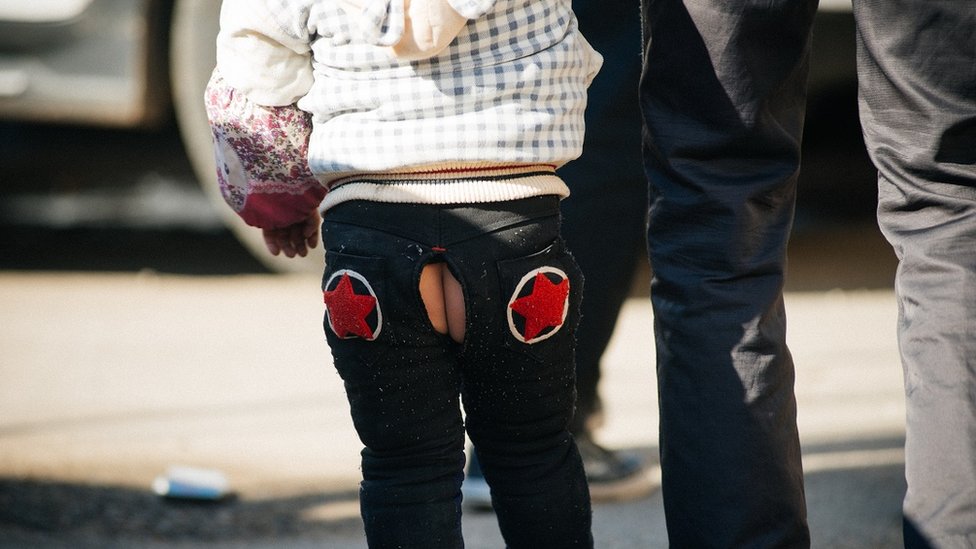 Niño en la calle usando un pantalón abierto.
