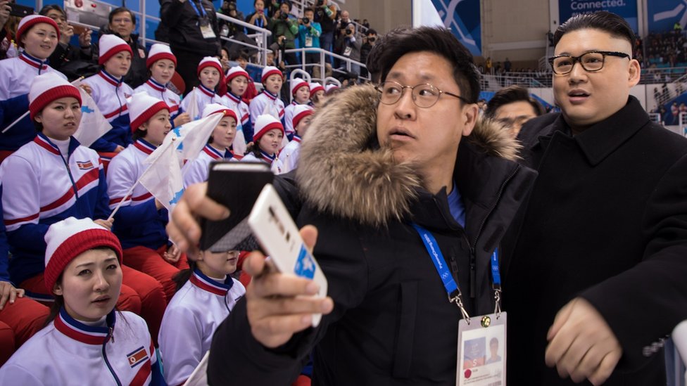 Some cheerleaders look at a Kim Jong-un impersonator disapprovingly whilst others look at the hockey match
