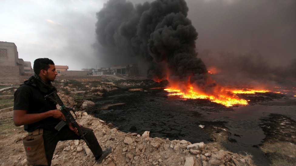 Un miembro de las fuerzas de seguridad observa el fuego y el humo que salen de un pozo petrolero incendiado por miembros de EI en Irak.