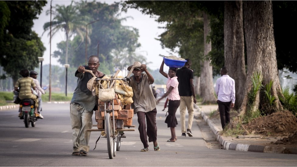 Hombres empujando bicicletas cargadas al máximo en las calles de Kananga