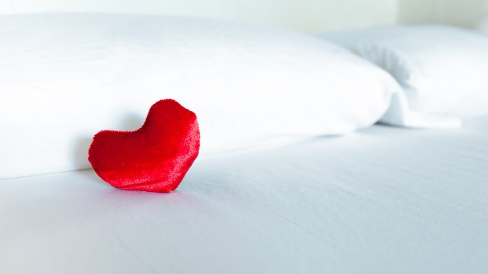 Corazón rojo sobre una cama blanca.