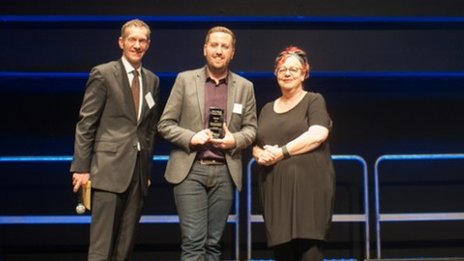 Ben on stage at the Mind Media Awards being handed his award by BBC Deputy News Editor Toby Castle and Jo Brand