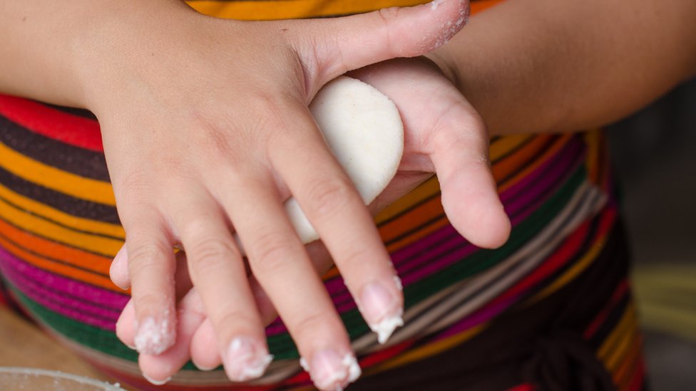 Una mujer amasada una harina de maíz para hacer arepas.