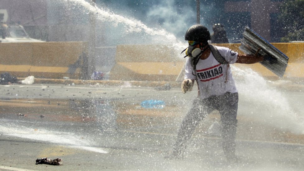 Manifestante recibe un chorro de agua de un carro hidrante.
