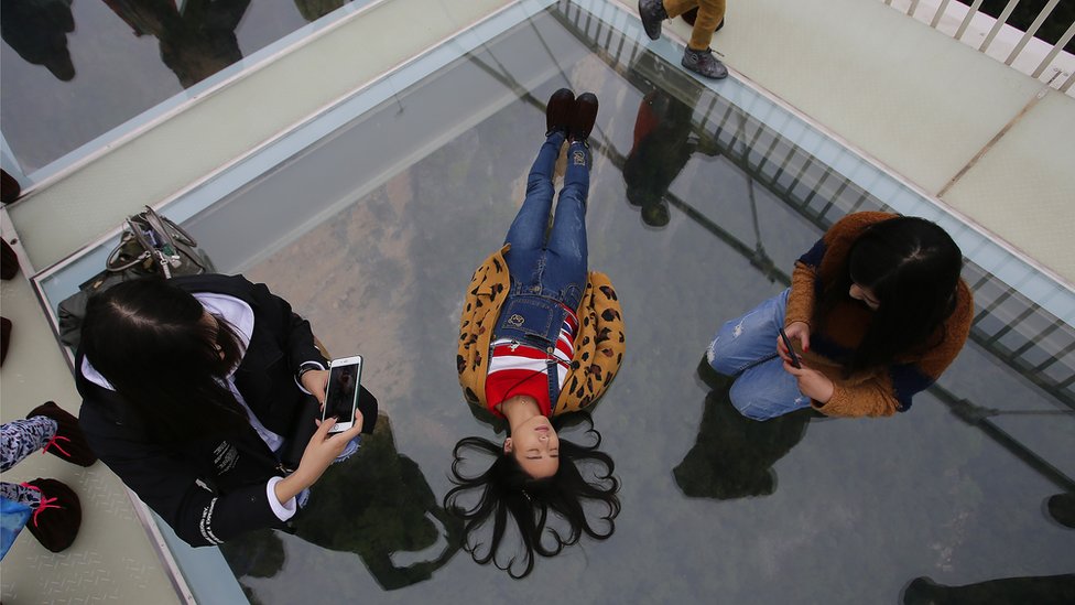 Una chica posa tumbada sobre un puente de cristal de China