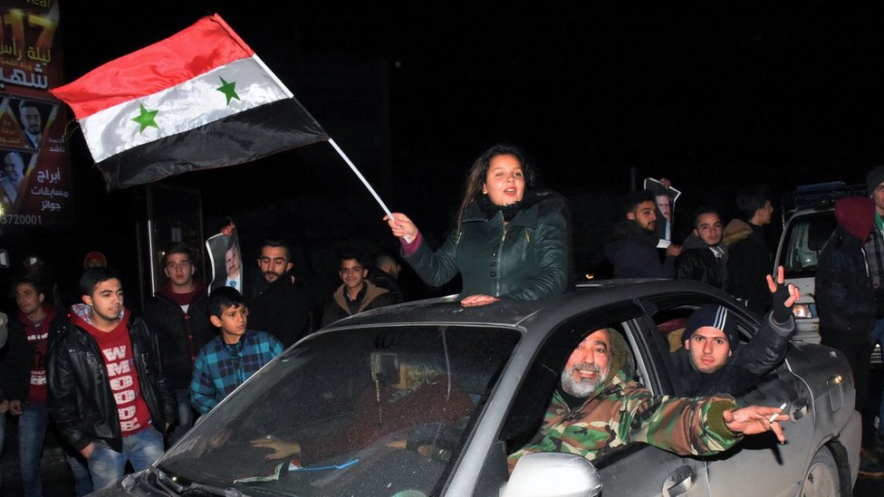 Mujer celebra con una bandera siria